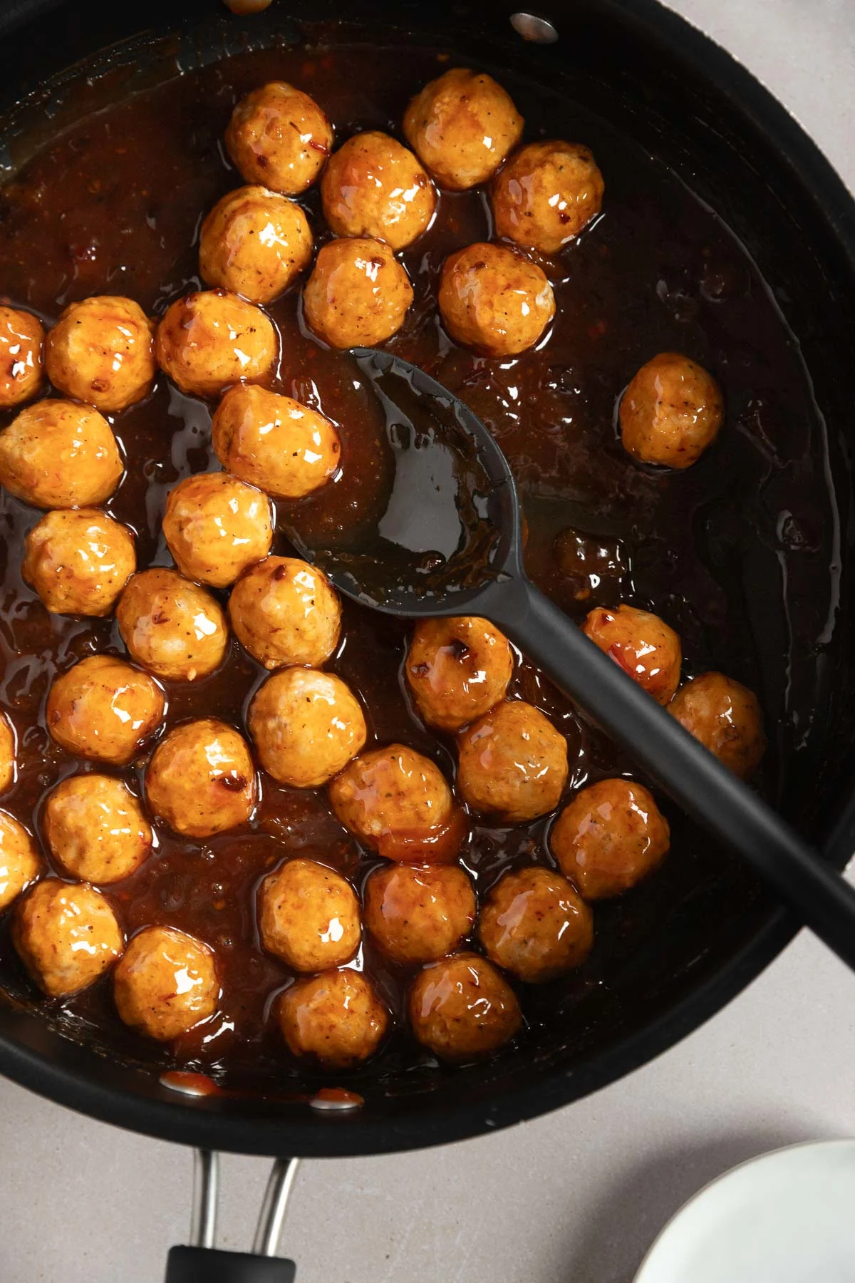 A black skillet filled with chipotle peach meatballs in a thick brown glaze, with a black slotted spoon resting among the meatballs.