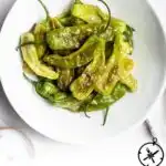 A white bowl filled with easy shishito peppers, drizzled with oil and sprinkled with salt, sits on a white surface. Text below the bowl reads, How to Cook Shishito Peppers, The Culinary Compass.
