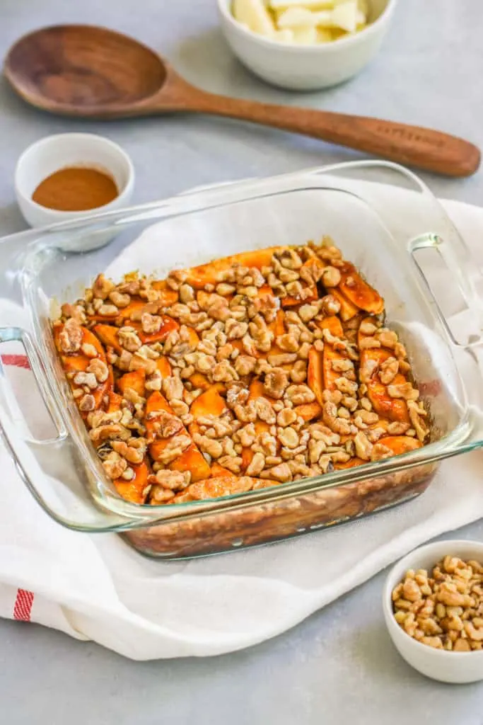 a container of apple strudel cake on a napkin with a small bowl of walnuts