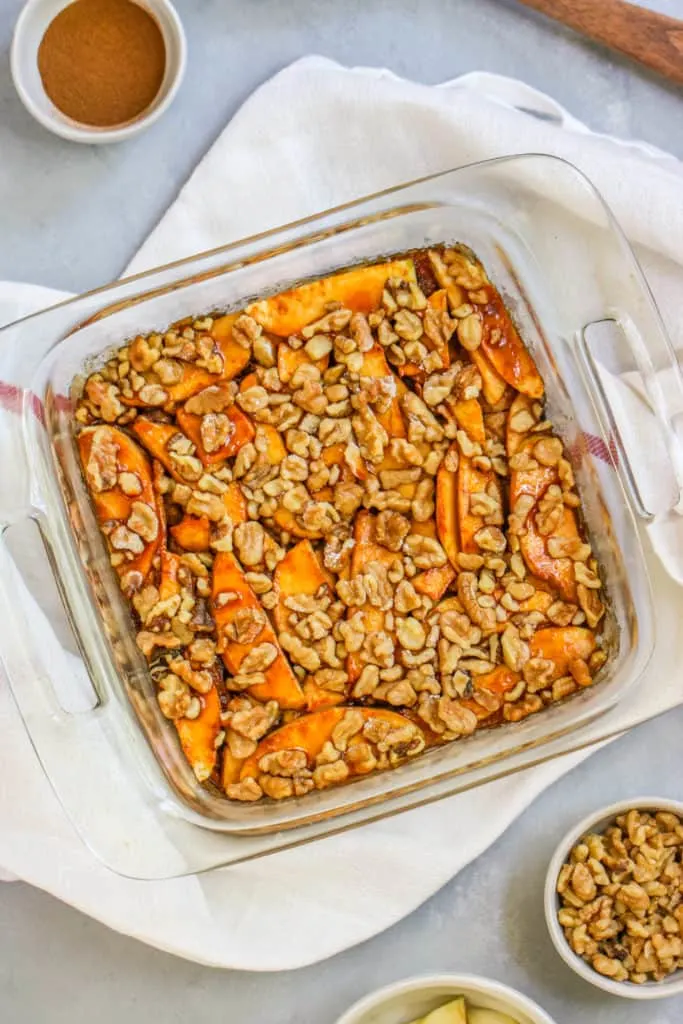 a container of apple strudel cake with a bowl of cinnamon and walnuts on the side