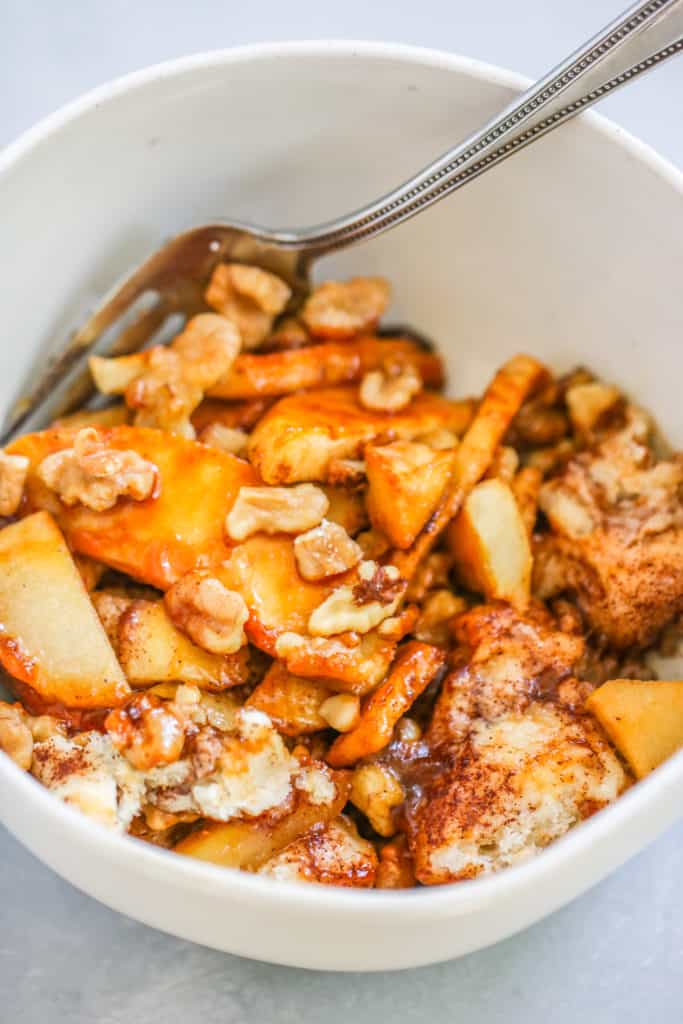 a bowl of apples, walnuts, and biscuit pieces with a fork