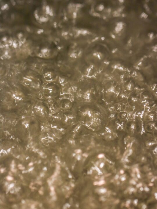 Close-up image of bubbling water, with numerous bubbles forming and rising to the surface—capturing the dynamic look often seen when making simple syrup.