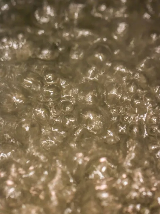 Close-up image of bubbling water, with numerous bubbles forming and rising to the surface—capturing the dynamic look often seen when making simple syrup.