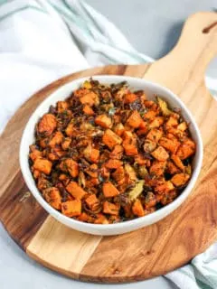 a bowl of roasted shaved brussels sprouts and sweet potatoes sitting on top of a wooden platter