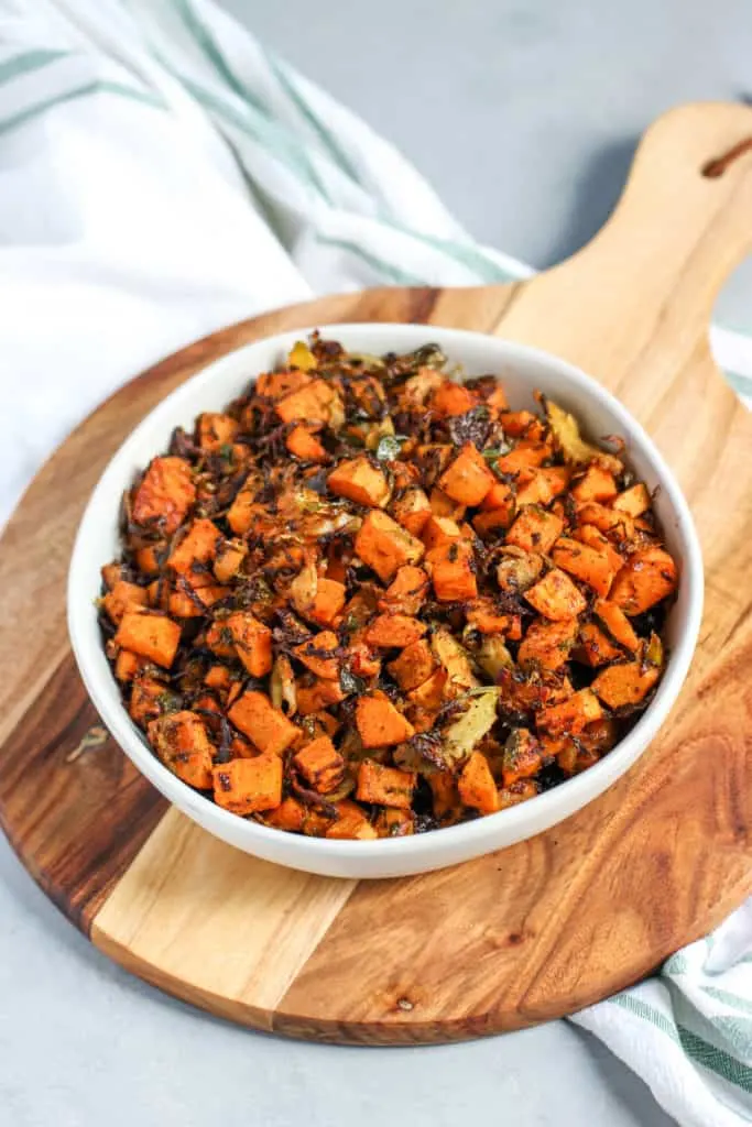 a bowl of roasted shaved brussels sprouts and sweet potatoes sitting on top of a wooden platter