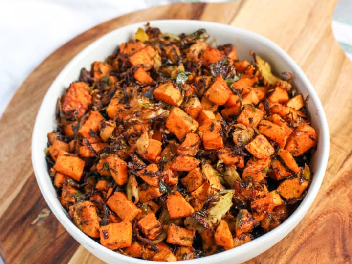 a bowl of roasted shaved brussels sprouts and sweet potatoes sitting on top of a wooden platter