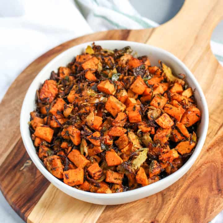 a bowl of roasted shaved brussels sprouts and sweet potatoes sitting on top of a wooden platter