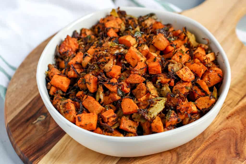 a close up image of a white bowl with roasted shaved brussels sprouts and sweet potatoes