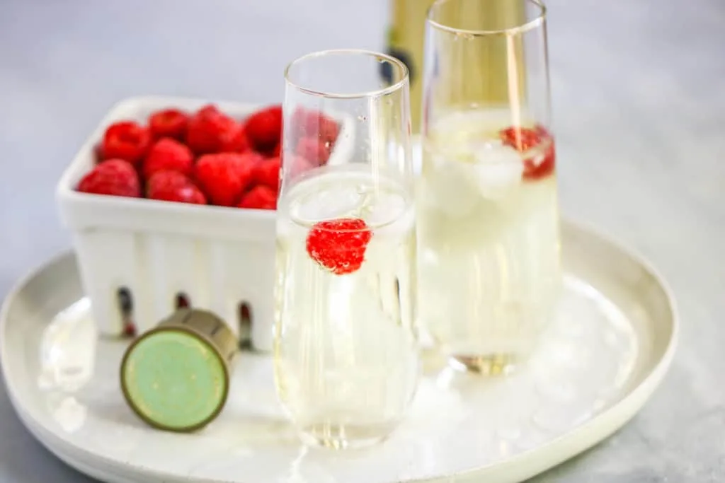 two stemless champagne flutes with the st. germain cocktail and a berry basket of raspberries