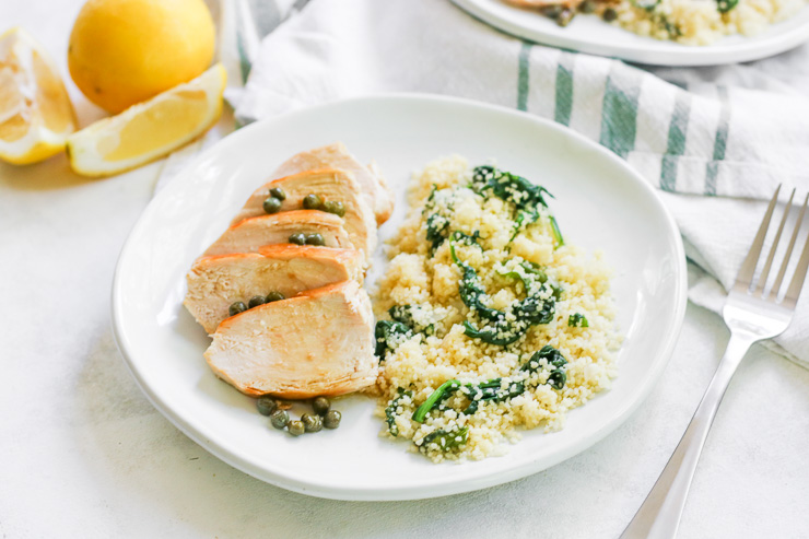 a horizontal image of the lemon caper chicken with a fork and lemon wedges beside the plate