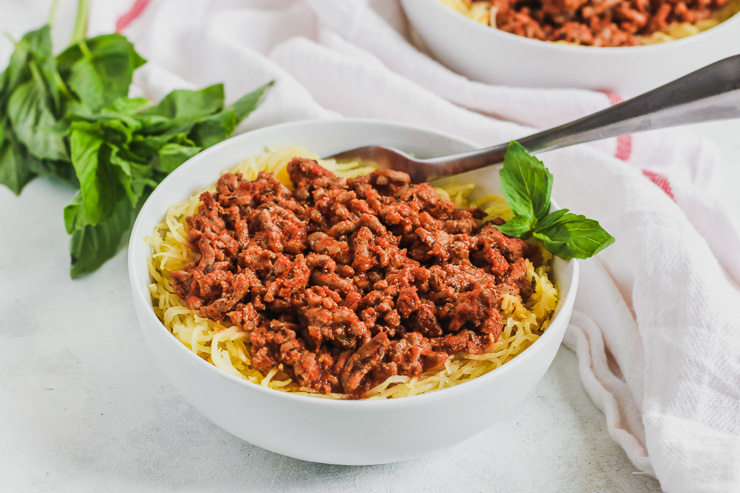 a close up image of a white bowl with Spaghetti Squash and Ground Turkey with a bunch of basil to the side