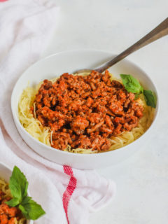 a white bowl with Spaghetti Squash and Ground Turkey and a white napkin with a red stripe