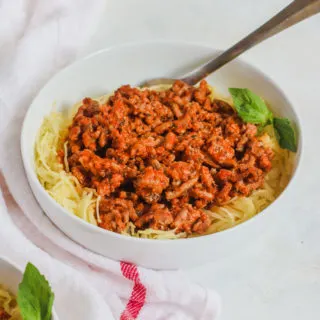 a white bowl with Spaghetti Squash and Ground Turkey and a white napkin with a red stripe