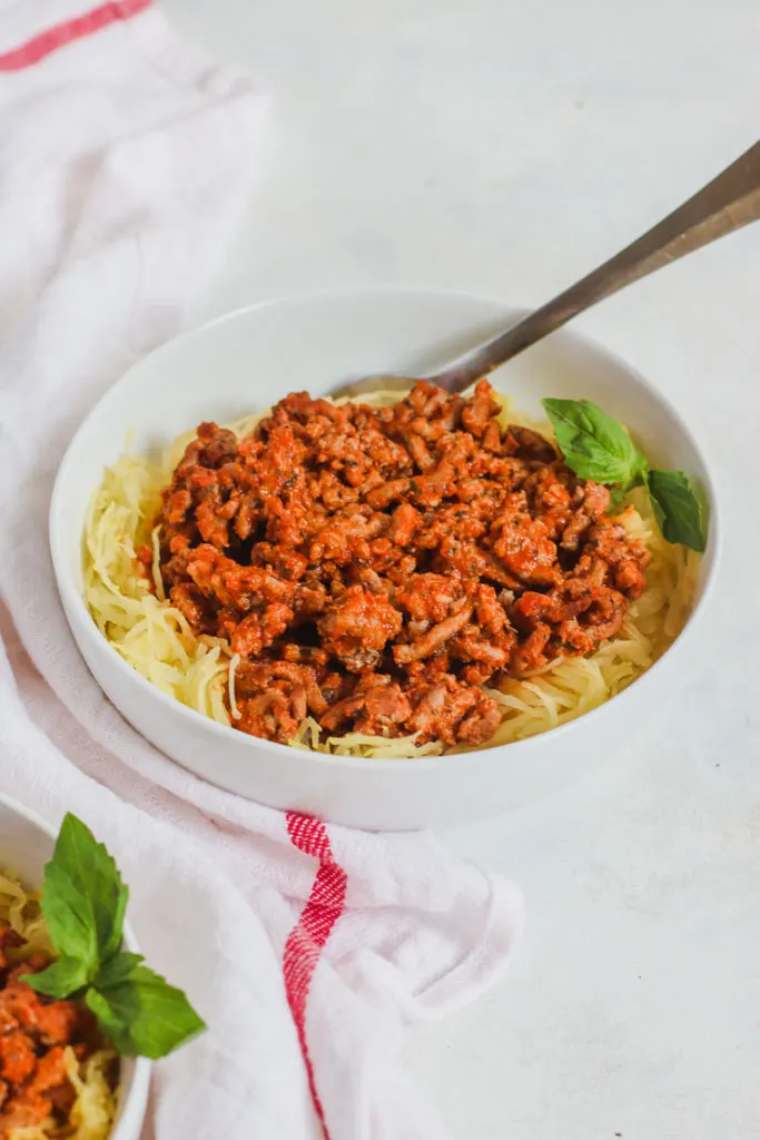 a white bowl with Spaghetti Squash and Ground Turkey and a white napkin with a red stripe