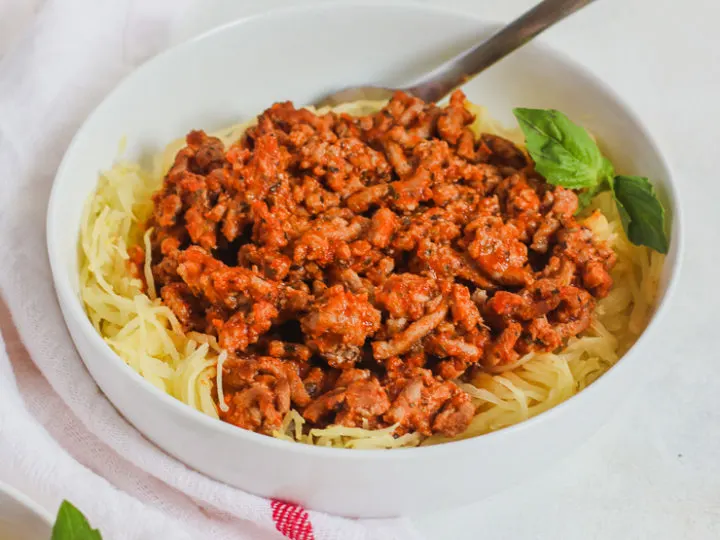 a white bowl with Spaghetti Squash and Ground Turkey and a white napkin with a red stripe