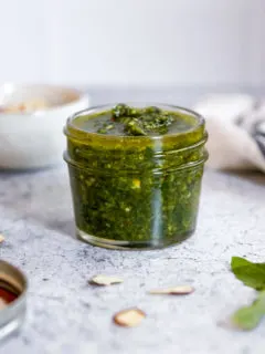 almond pesto in a jar surrounded by some ingredients