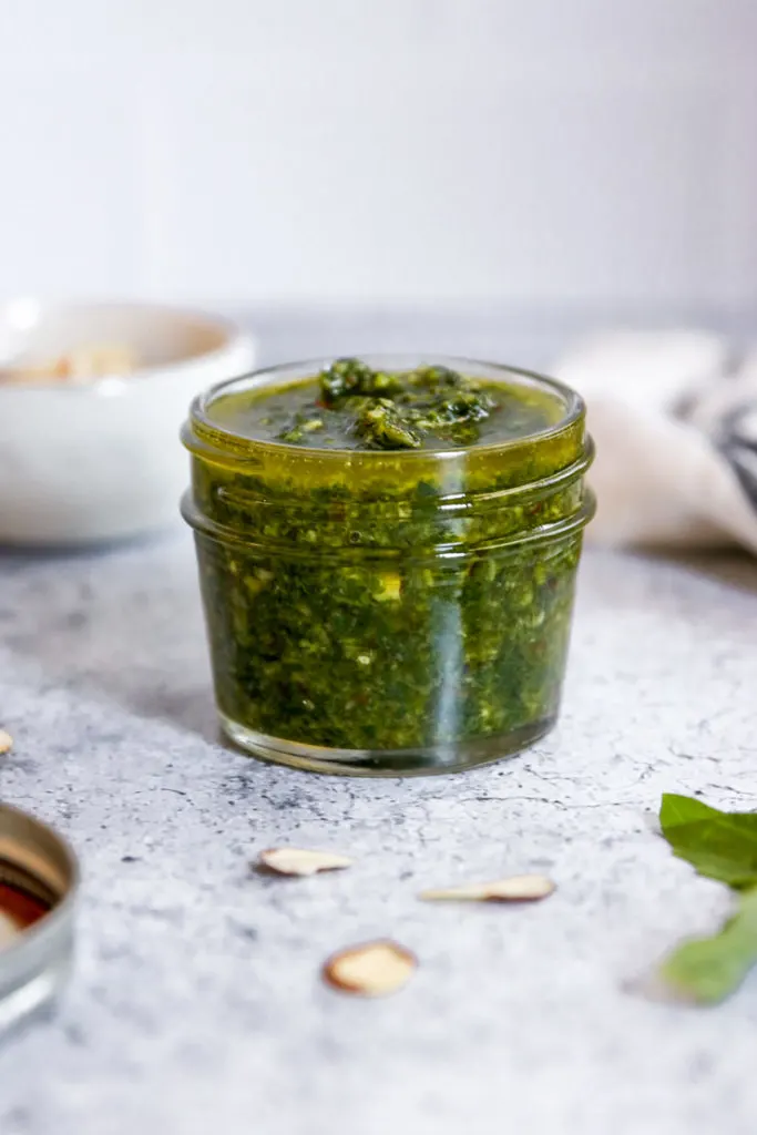 almond pesto in a jar surrounded by some ingredients