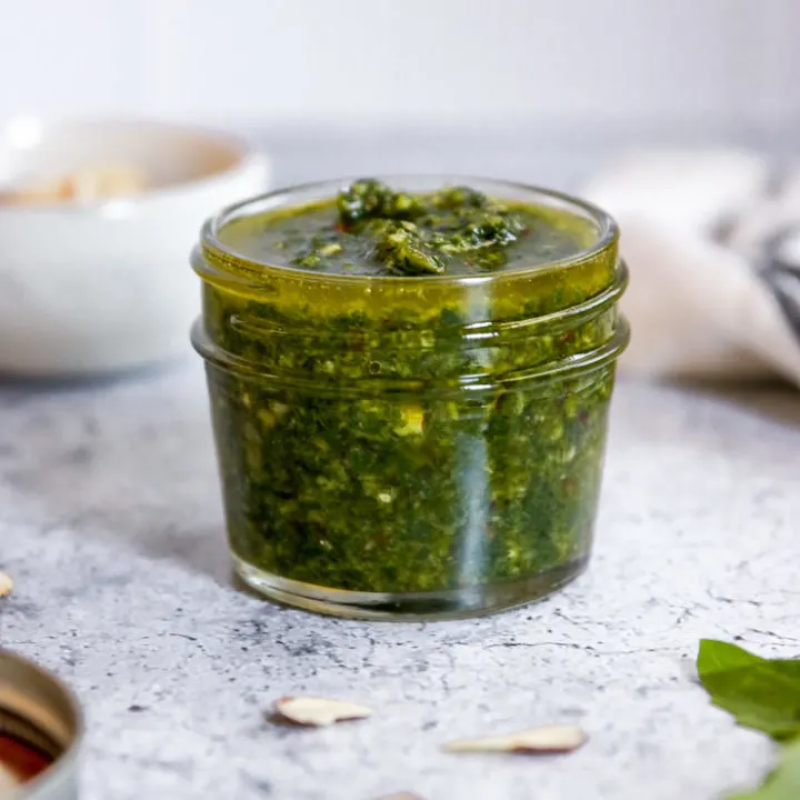 almond pesto in a jar surrounded by some ingredients