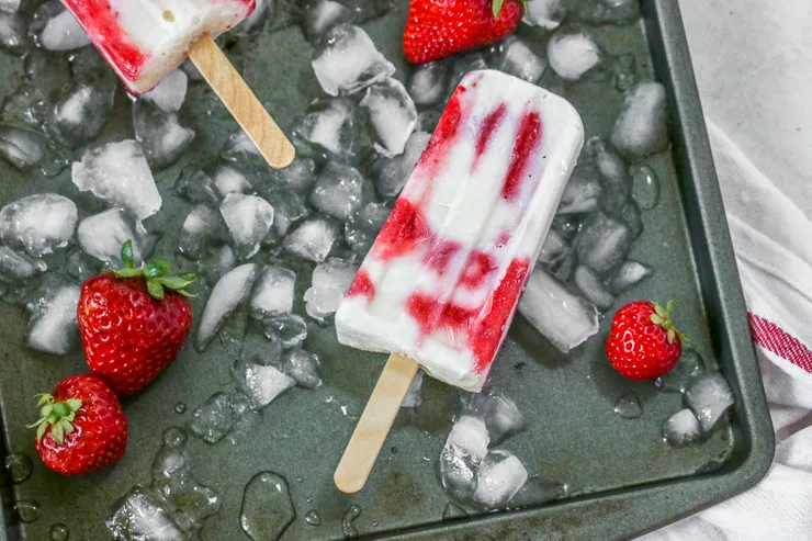 one strawberry yogurt popsicle on a cookie sheet with ice