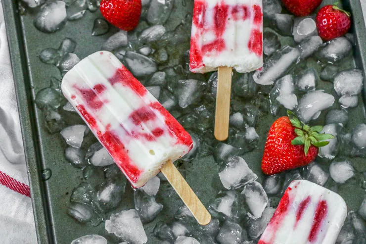 three strawberry yogurt popsicles on ice with strawberries