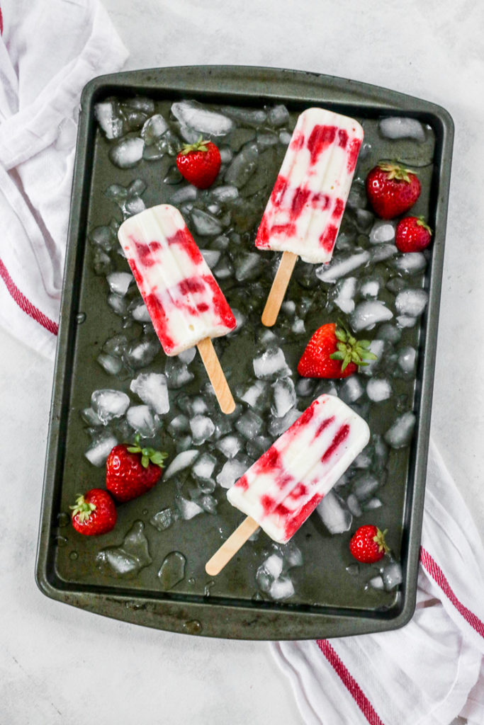 three strawberry yogurt popsicles on a pan with ice