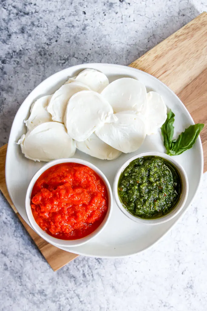 a plate of sliced mozzarella, vodka sauce and pesto