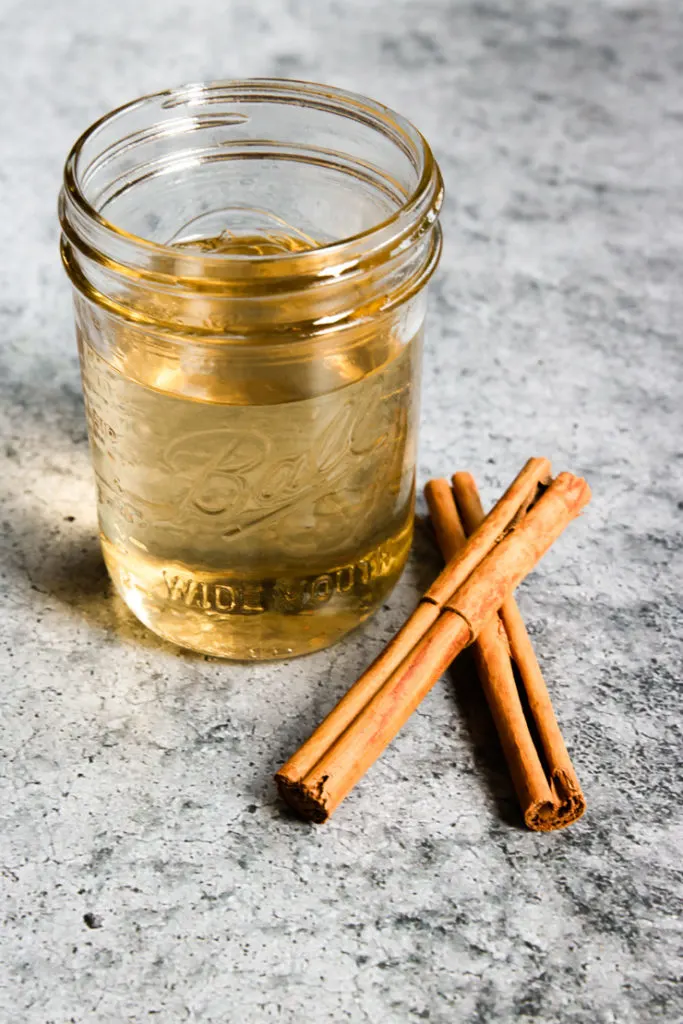 a mason jar of light brown syrup with cinnamon sticks next to it