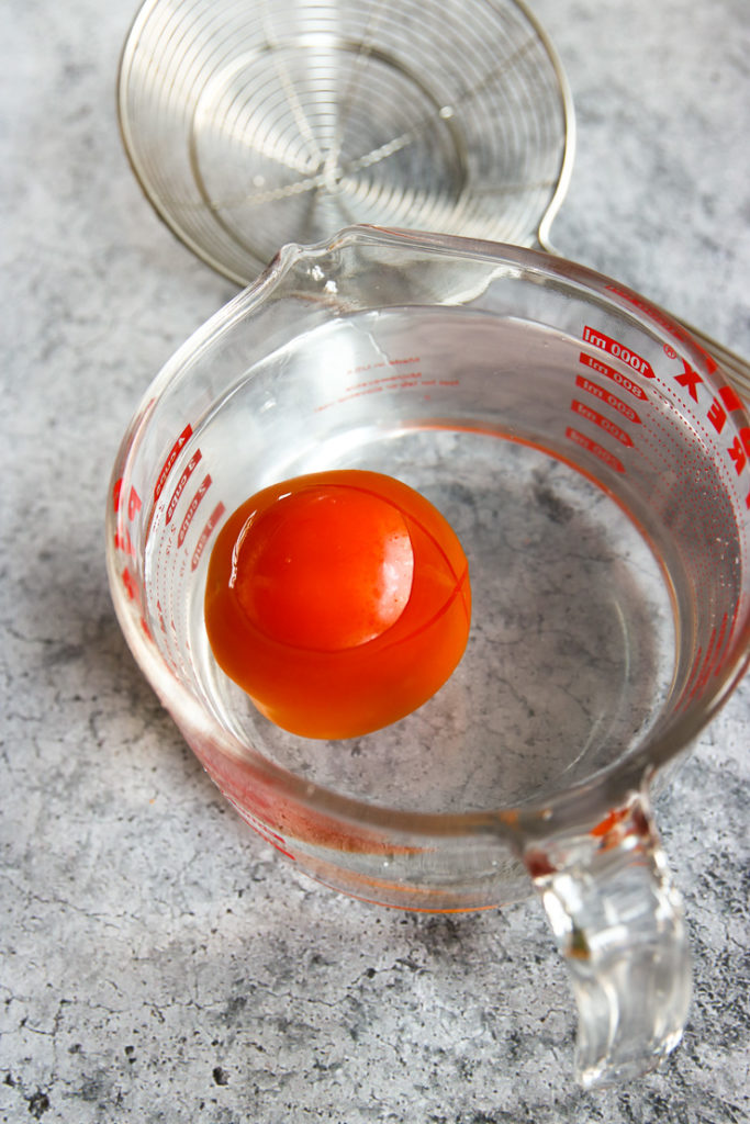 a tomato floating in water in a pyrex measuring cup