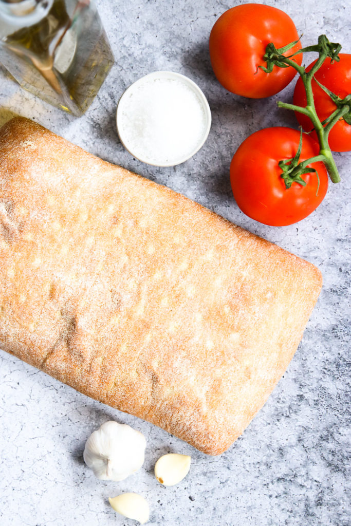 a ciabatta loaf, garlic cloves, olive oil, salt, and tomatoes on the vine