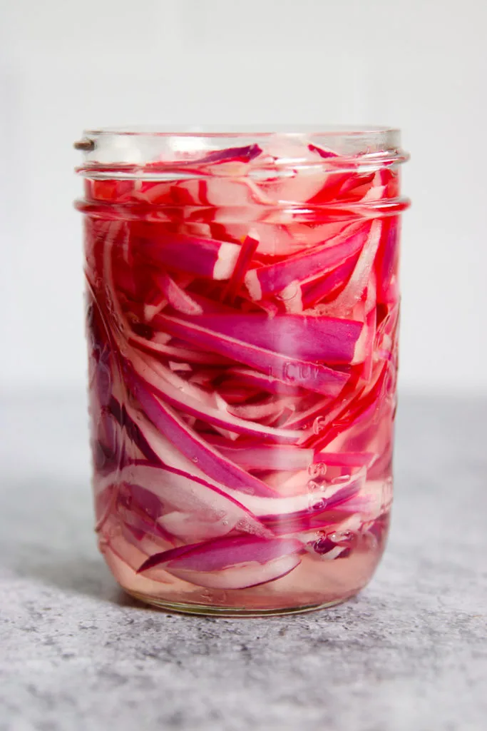 a mason jar of red onions with vinegar added