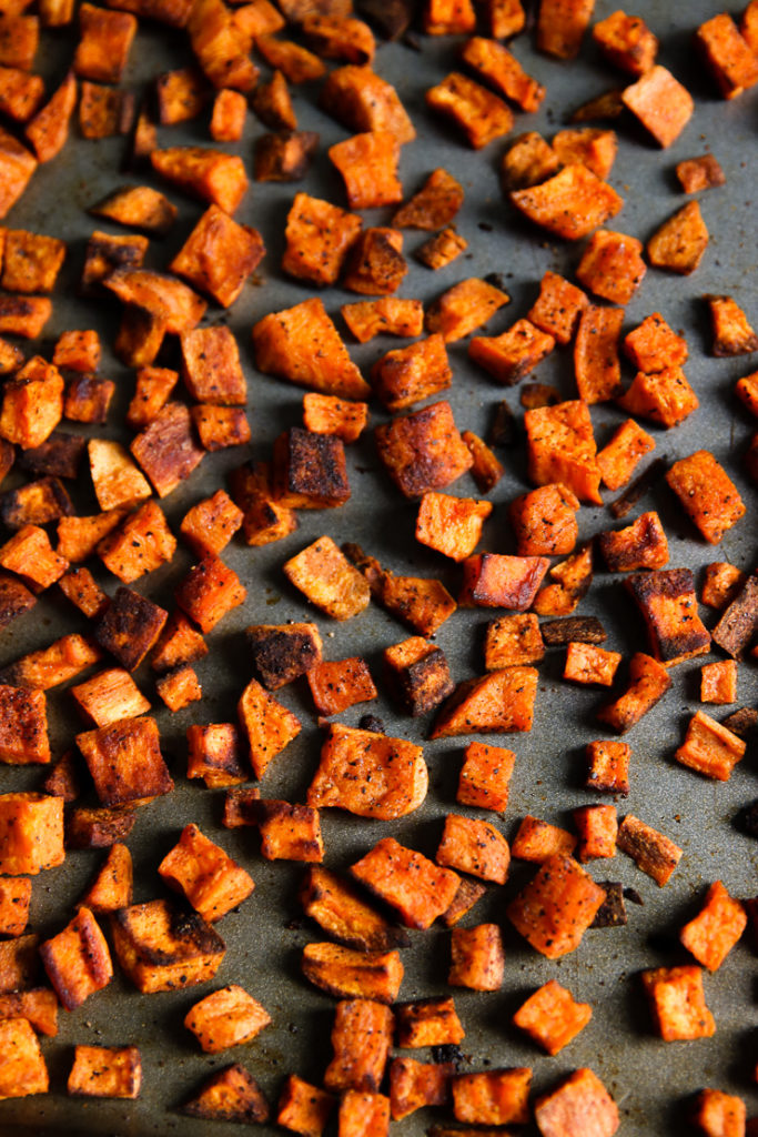 An overhead shot of chopped crispy roasted sweets potatoes on a baking sheet