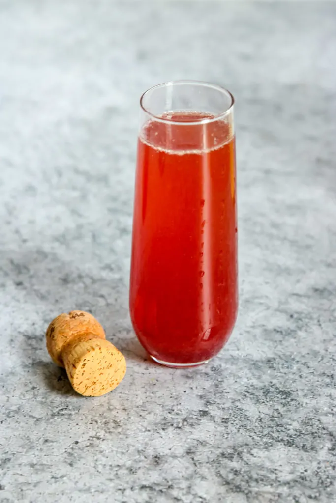 A glass of Pomegranate Mimosa next to a champagne cork