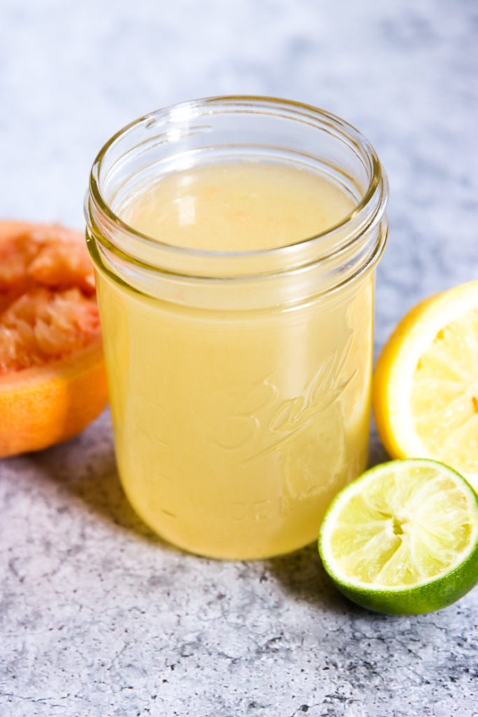 A mason jar full of Homemade Sour Mix surrounded by squeezed citrus fruit