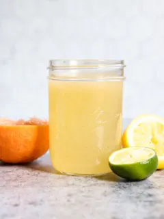 A side view of a mason jar filled with Homemade Sour Mix and squeezed citrus fruit