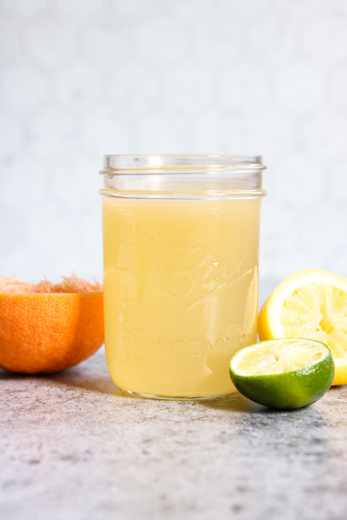 A side view of a mason jar filled with Homemade Sour Mix and squeezed citrus fruit