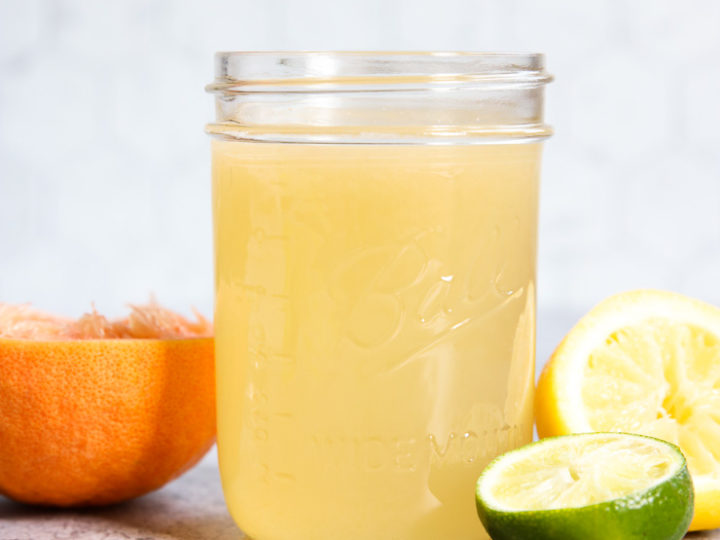 A side view of a mason jar filled with Homemade Sour Mix and squeezed citrus fruit