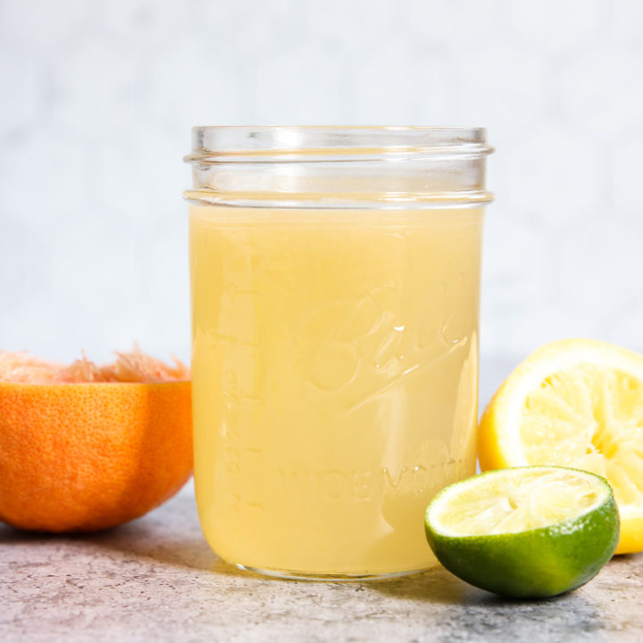 A side view of a mason jar filled with Homemade Sour Mix and squeezed citrus fruit