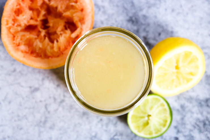 an overhead shot of a mason jar of homemade sour mix and squeezed citrus