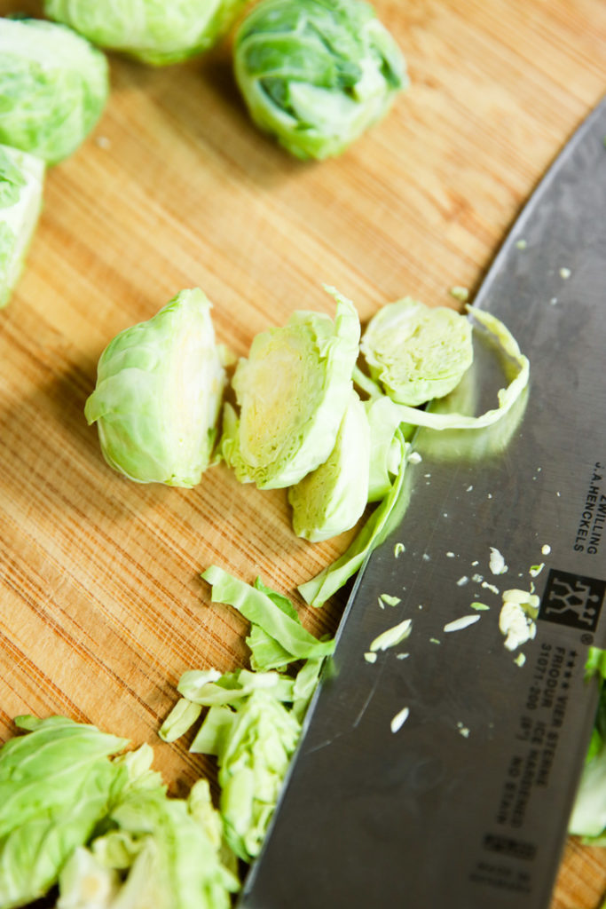 Sliced Brussels Sprouts and a knife on a wooden cutting board