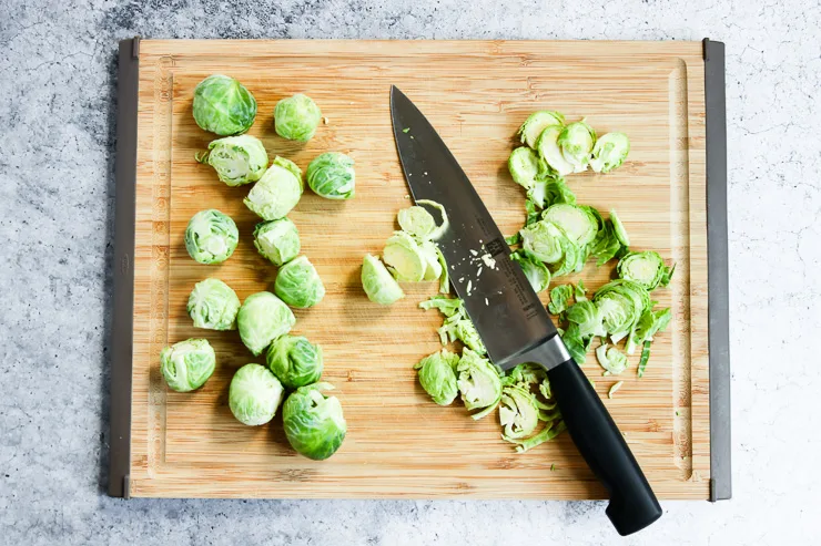 thinly slicing pieces of brussels sprouts with a knife on a cutting board