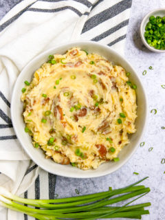 an overhead shot of red skin mashed potatoes and a few stalks of green onions next to a striped napkin