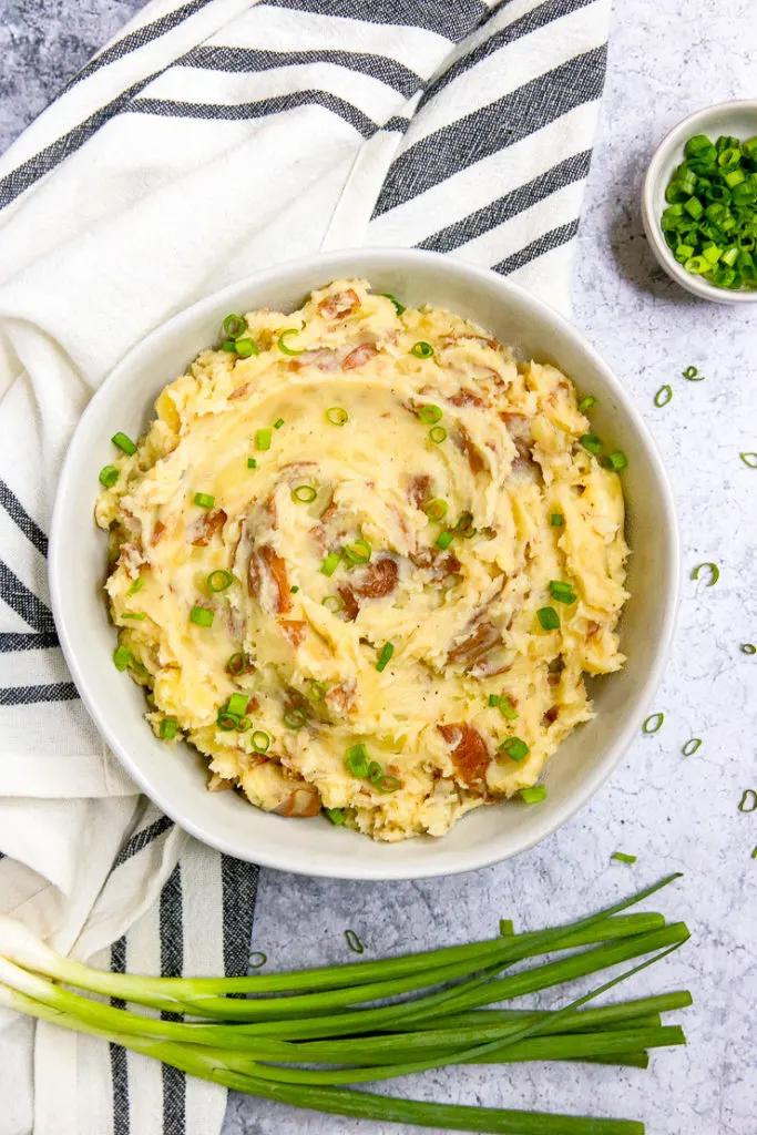 an overhead shot of red skin mashed potatoes and a few stalks of green onions next to a striped napkin