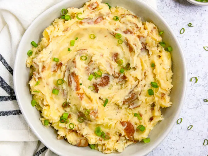 an overhead shot of red skin mashed potatoes and a few stalks of green onions next to a striped napkin