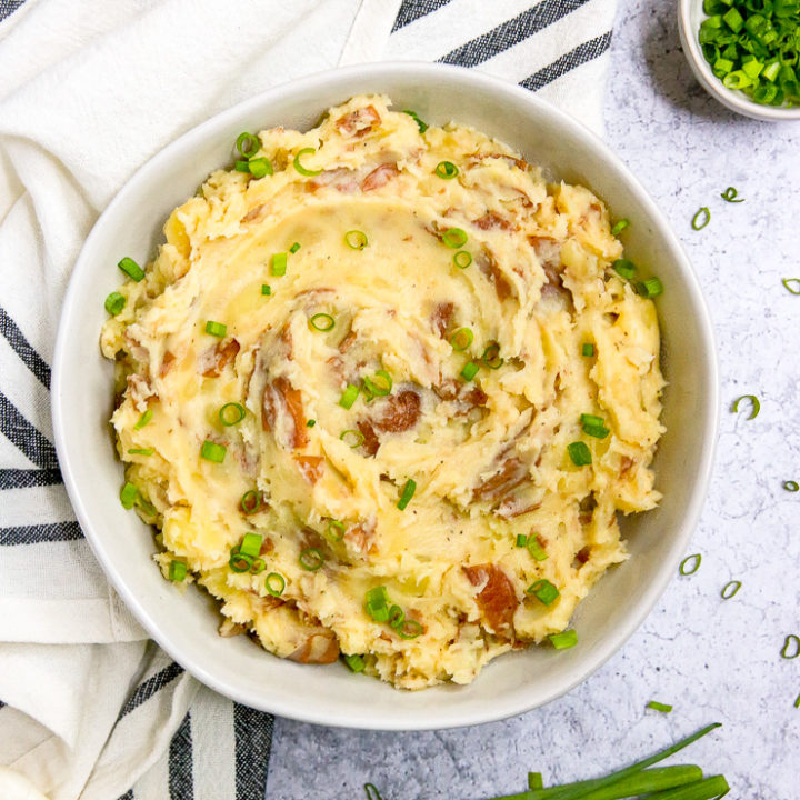 an overhead shot of red skin mashed potatoes and a few stalks of green onions next to a striped napkin