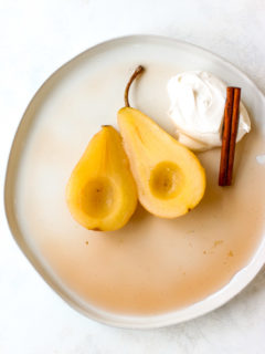 a plate of two halves of poached pears with whipped cream and a cinnamon stick