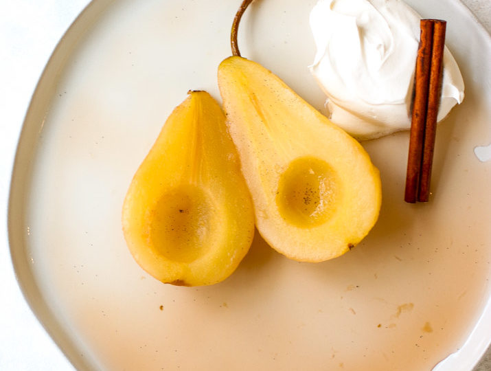 a plate of two halves of poached pears with whipped cream and a cinnamon stick