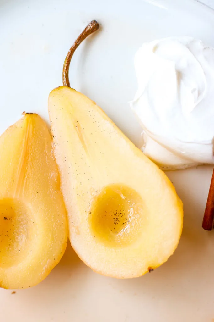 a close up of a halved pear with vanilla bean seeds and whipped cream