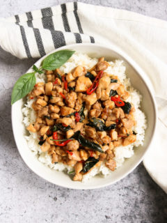 an overhead shot of a bowl of thai basil chicken over rice with a sprig of thai basil