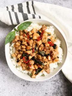 an overhead shot of a bowl of thai basil chicken over rice with a sprig of thai basil