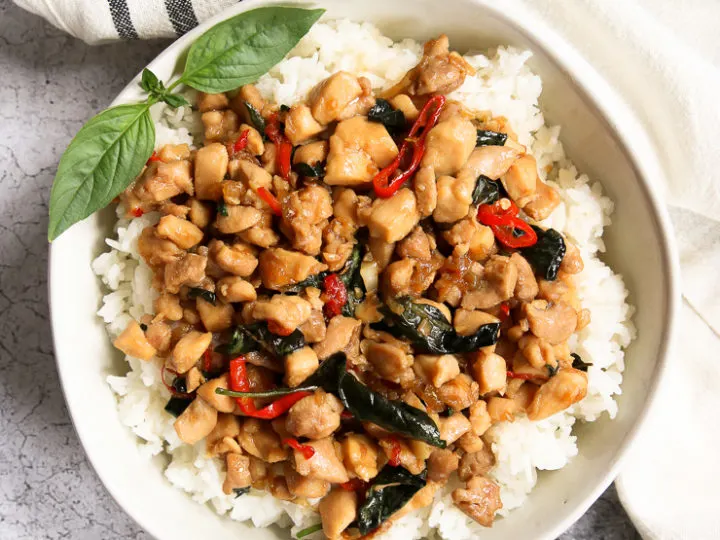 an overhead shot of a bowl of thai basil chicken over rice with a sprig of thai basil